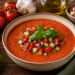 Kalte Gazpacho aus sonnengereiften Tomaten, Gurken, Paprika und Zwiebeln, serviert in einer rustikalen Schale und garniert mit frischen Gemüsestückchen sowie Basilikum.