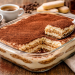 Cremiges klassisches Tiramisu in einer Glasform, geschichtet aus Mascarponecreme und in Espresso getränkten Löffelbiskuits, mit Kakao bestäubt, serviert auf rustikalem