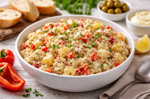 Cremige Ensaladilla in einer Schüssel – spanischer Brotaufstrich mit Kartoffeln und Thunfisch, Paprika, Karotten, Ei und Mayonnaise, serviert auf rustikalem Tisch im Querformat.