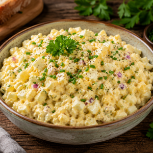 Hausgemachter Eiersalat mit gewürfelten Eiern, roten Zwiebeln, frischem Schnittlauch und cremigem Dressing in einer rustikalen Schale auf einem Holztisch angerichtet.