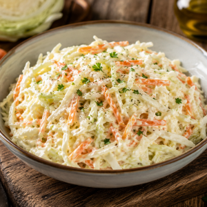 Frischer Krautsalat mit fein geschnittenem Weißkohl und Karotten in cremigem Dressing, serviert in einer Schale auf rustikalem Holztisch mit frischen Kräutern und Gemüse.