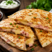 Knusprige Schinken-Käse-Quesadillas mit geschmolzenem Käse und herzhaftem Kochschinken, goldbraun gebraten und auf einem rustikalen Holzbrett mit Dip serviert.