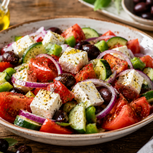 Frischer griechischer Bauernsalat mit Tomaten, Gurken, roten Zwiebeln, grüner Paprika, schwarzen Oliven und Feta, serviert in einer rustikalen Schale mit Olivenöl und mediterranen Kräutern.