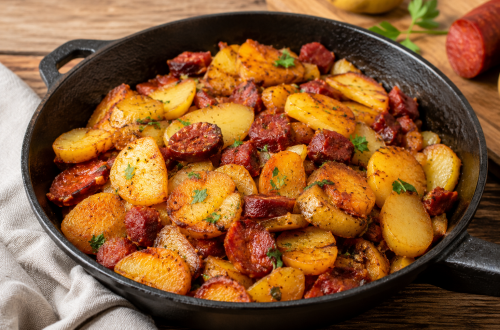 Knusprige Bratkartoffeln mit würziger Chorizo in einer gusseisernen Pfanne, goldbraun gebraten und mit frischen Kräutern garniert auf rustikalem Holztisch serviert.