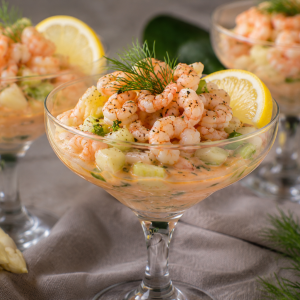 Krabben-Spargelcocktail in eleganten Cocktailgläsern mit zarten Garnelen, weißem Spargel, cremigem Dressing, frischem Dill und Zitronenscheiben. Arrangiert auf einem festlich gedeckten Tisch mit Spargelstangen und Kräutern. Fotorealistische Darstellung einer klassischen Vorspeise mit Krabben und Spargel.