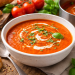 Fotorealistische Aufnahme einer cremigen Tomatensuppe in einer hellen Keramikschale auf rustikalem Holztisch, garniert mit Sahneswirbel und frischem Basilikum, serviert mit Baguette und frischen Tomaten.