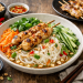 Fotorealistischer vietnamesischer Nudelsalat mit Reisnudeln, gegrillten Hähnchenspießen, Gurkenstreifen, Karotten, frischem Koriander und gehackten Erdnüssen in einer Schale, serviert mit würzigem Dressing auf rustikalem Holztisch