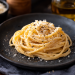 Fotorealistische Spaghetti Carbonara auf einem dunklen Keramikteller, cremig angerichtet und mit geriebenem Pecorino sowie frisch gemahlenem schwarzem Pfeffer verfeinert. Serviert auf einem rustikalen Holztisch mit stimmungsvoll unscharfem Hintergrund im italienischen Stil. 🍝🇮🇹