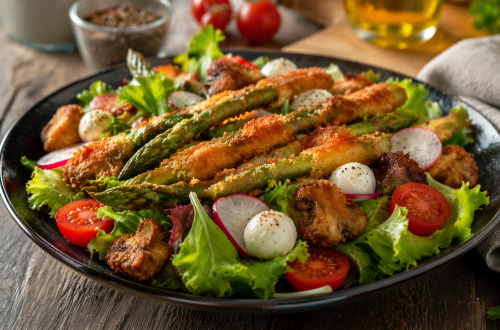 Frischer Frühlingssalat mit knusprig gebackenem Spargel, Champignons, Cocktailtomaten, Mini-Mozzarella und Radieschen auf einem Teller angerichtet