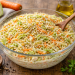 Glas-Schüssel mit cremigem Krautsalat aus fein geschnittenem Spitzkohl, Karotten und Zwiebeln auf einem Holztisch, daneben Öl, Gewürze und frische Zutaten.