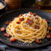 Cremige Spaghetti Carbonara auf einem dunklen Keramikteller, mit knusprig gerösteten Guanciale-Würfeln, geriebenem Pecorino und frisch gemahlenem schwarzem Pfeffer angerichtet.