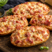 Pizza-Weckle mit Schinken, Salami und geschmolzenem Käse, knusprig im Ofen überbacken und auf einem rustikalen Holzbrett serviert.