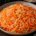 Karottensalat mit Glasnudeln, fein gehobelten Karotten, etwas gepresstem Knoblauch, Chili und schwarzem Pfeffer in einer rustikalen Schale.