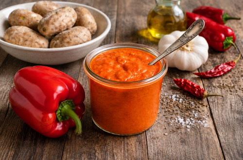 Rote Mojo Soße (Mojo Rojo) im Glas mit roten Paprika, Knoblauch, getrockneten Chilischoten und kanarischen Kartoffeln auf einem rustikalen Holztisch.