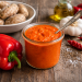 Rote Mojo Soße (Mojo Rojo) im Glas mit roten Paprika, Knoblauch, getrockneten Chilischoten und kanarischen Kartoffeln auf einem rustikalen Holztisch.